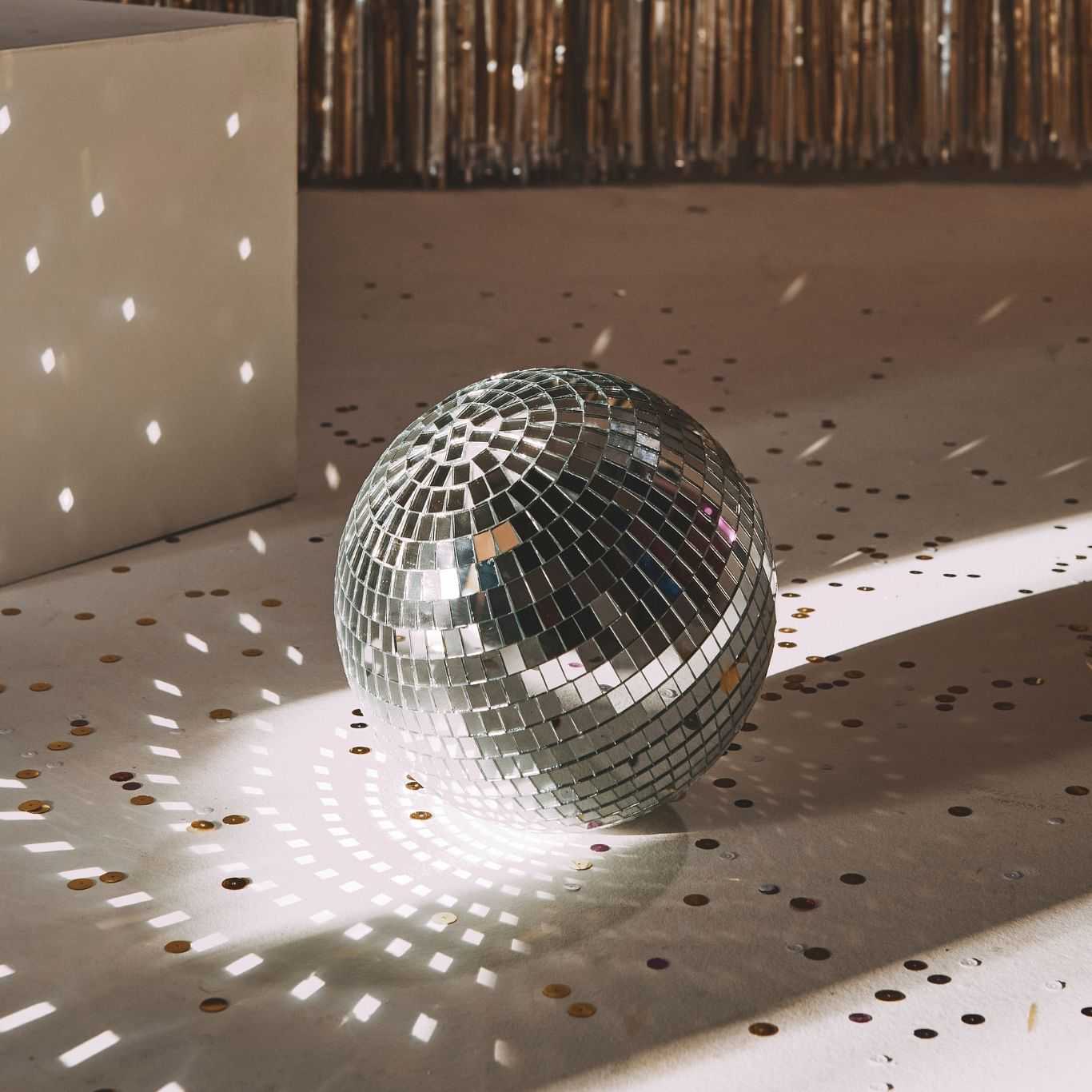 Shiny disco ball on a confetti-strewn floor with shimmering curtain backdrop.