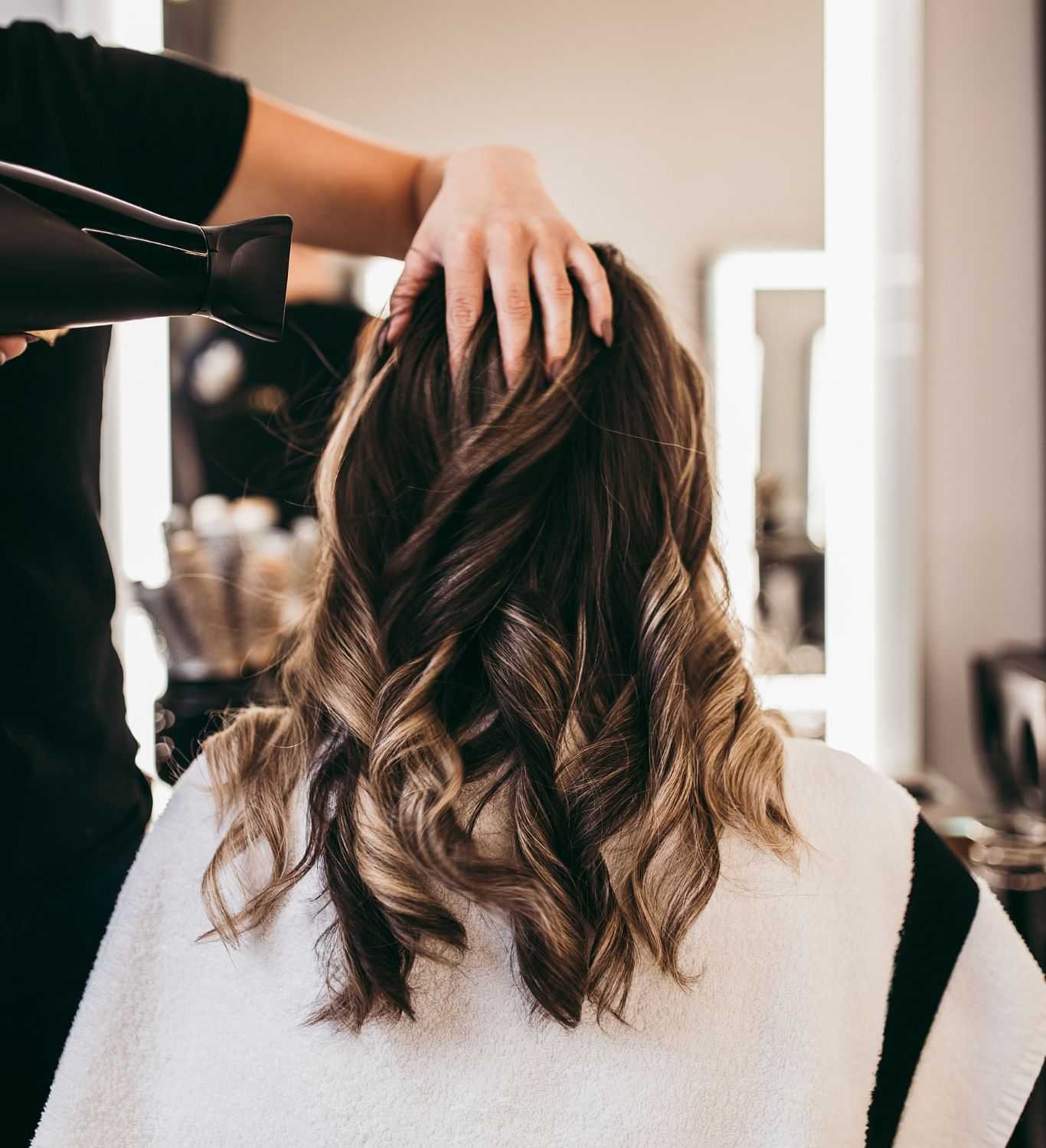 Hairdresser styling wavy, brown hair in a salon.